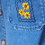 Motifs brodés sur une veste en jeans : tournesol entouré d'un motif rappelant le tour d'un timbre.